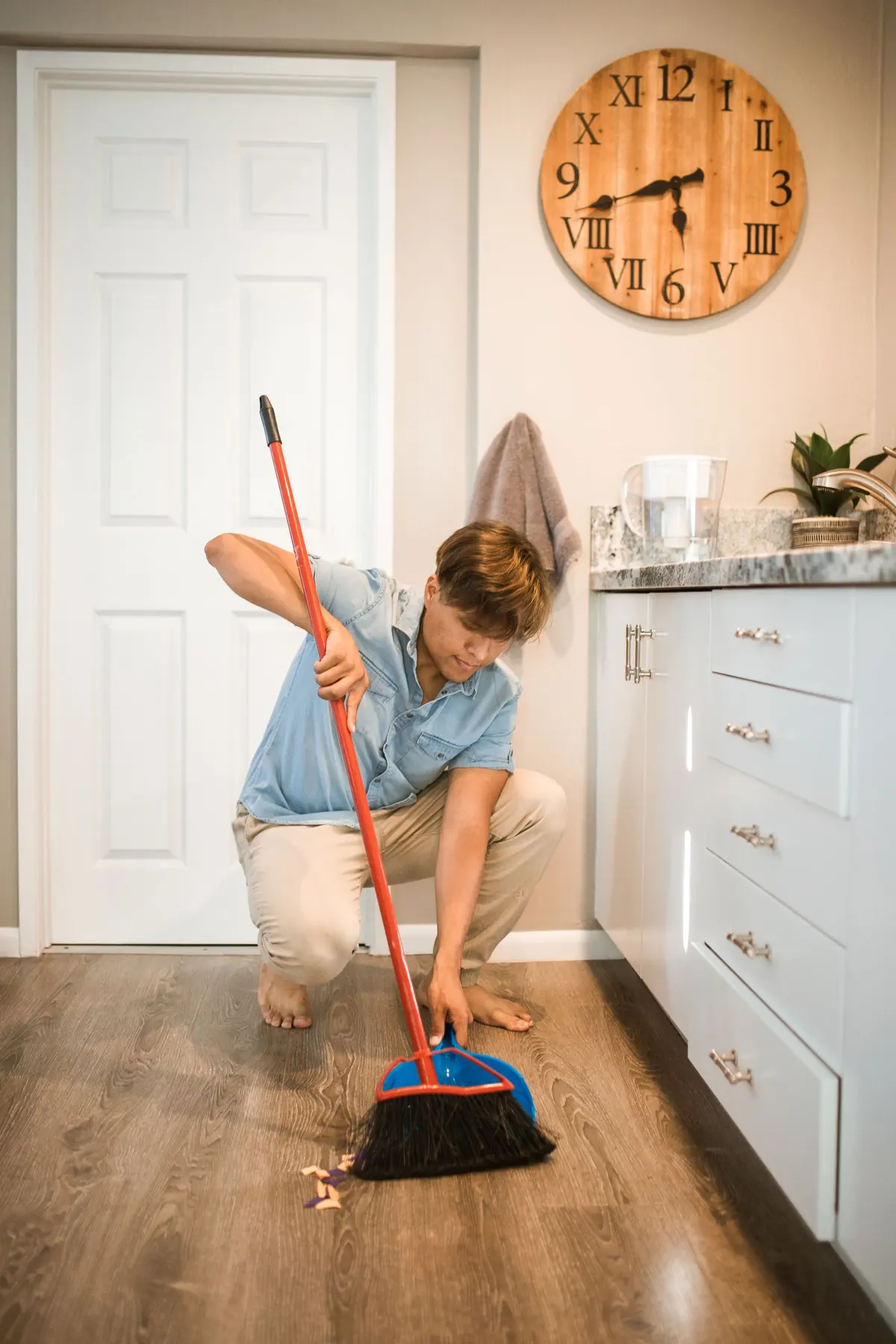 Person sweeping a wood-look luxury vinyl plank floor beside white kitchen cabinets